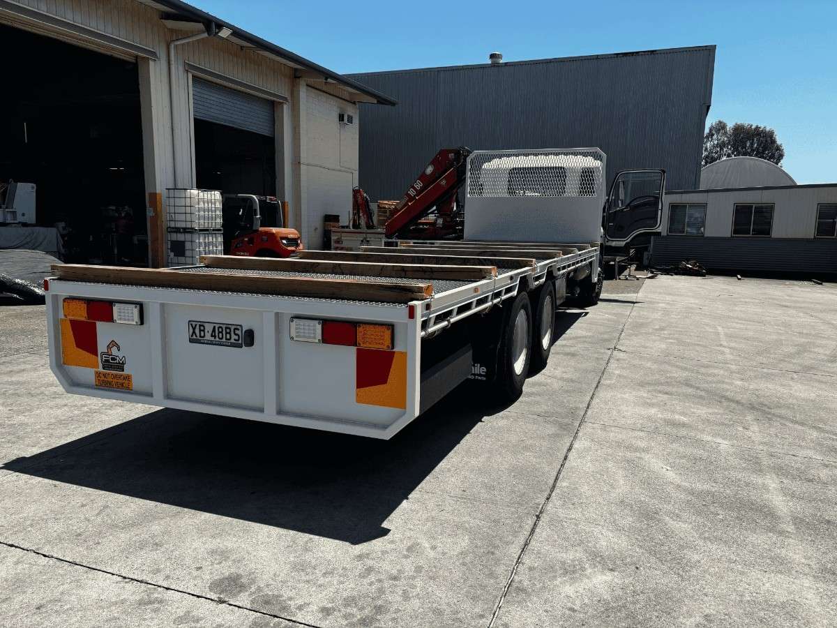 Customised FCM truck tray with timber guides, mesh headboard and multi-axle setup, parked in industrial depot yard.