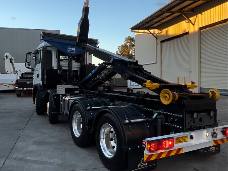 Rear view of tri-axle truck fitted with HSR hooklift installed by FMC, showing lifting arm and reinforced chassis.