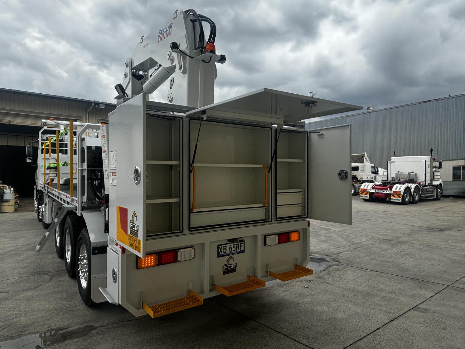Flatbed truck with Stellar TM16160 tyre handler and FCM logo, featuring open rear toolbox and yellow entry steps.