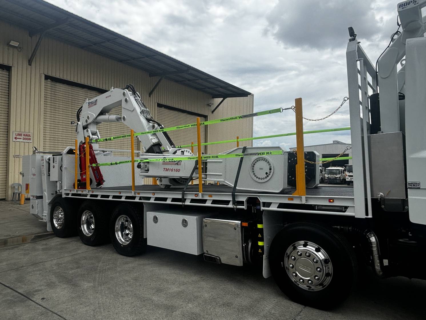 Close side view of a Stellar TM16160 tyre handler mounted on a flatbed truck, secured with green straps and safety rails.