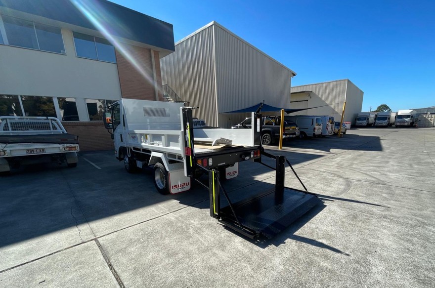 Truck with raised tailgate lift platform positioned for cargo loading in an outdoor industrial yard.