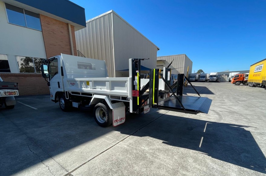 Truck with tailgate lift fully extended to the ground, positioned in an outdoor yard.